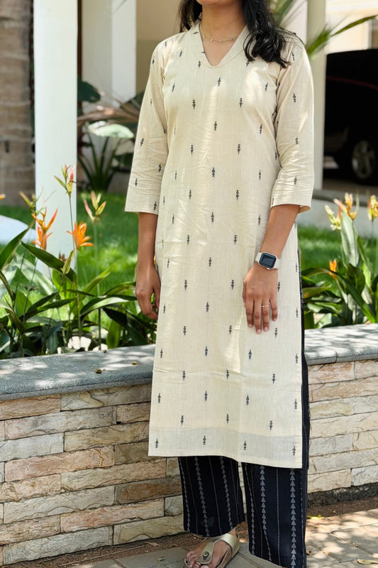 Woman in a white kurta with black pants standing outdoors near a building and plants.