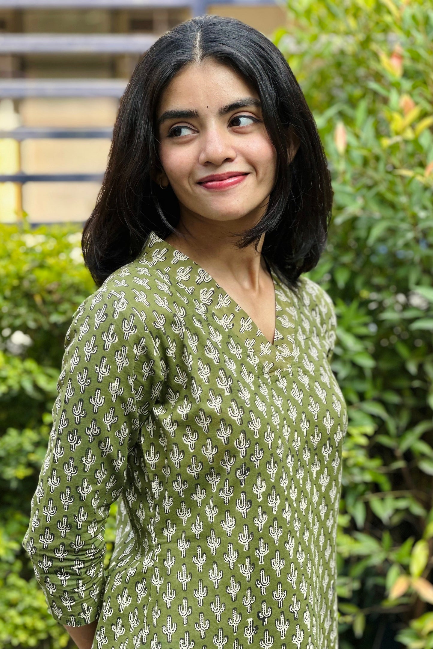 Woman wearing a green patterned top outdoors with greenery in the background