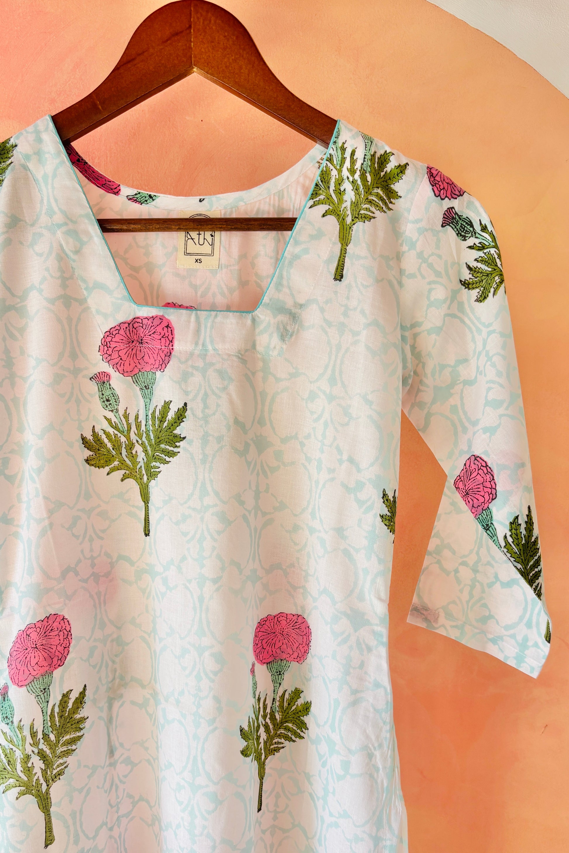 Floral printed top on a hanger against a peach background