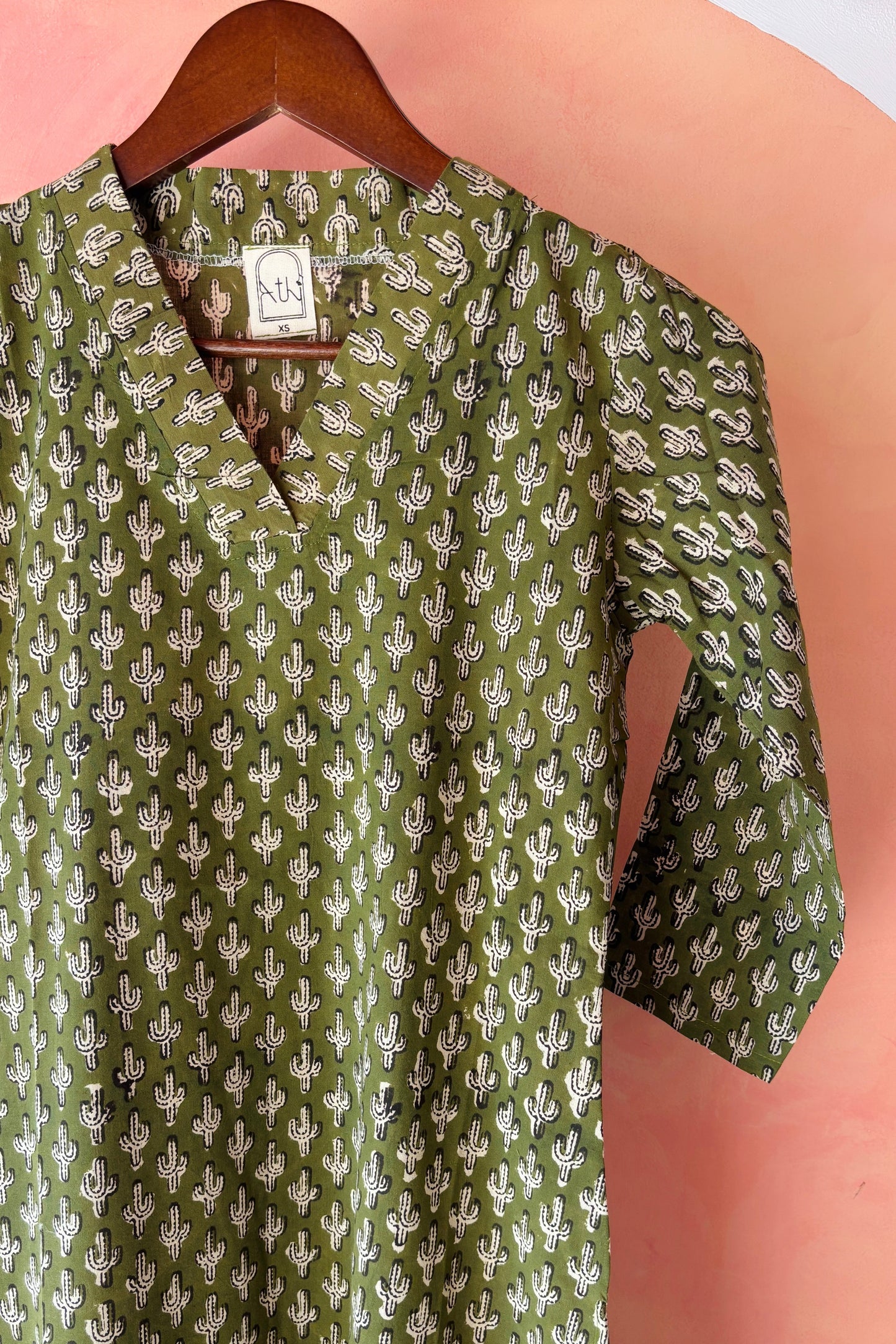 Green dress with white cactus pattern on a hanger against a pink background