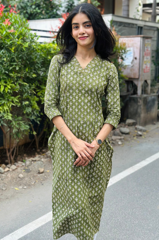 Woman in a green patterned dress standing on a street with plants in the background