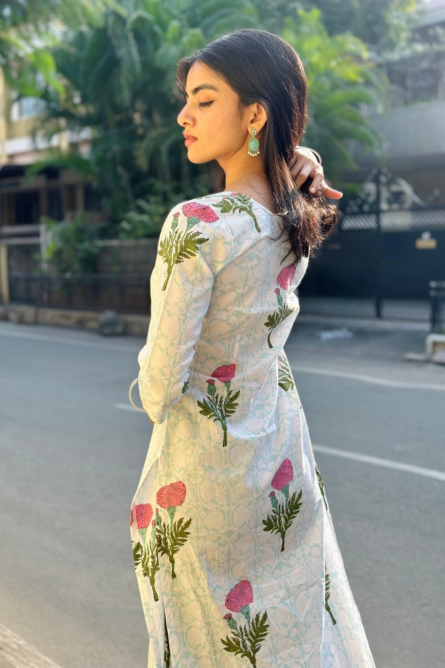 Woman in a floral kurta standing on a street with greenery in the background