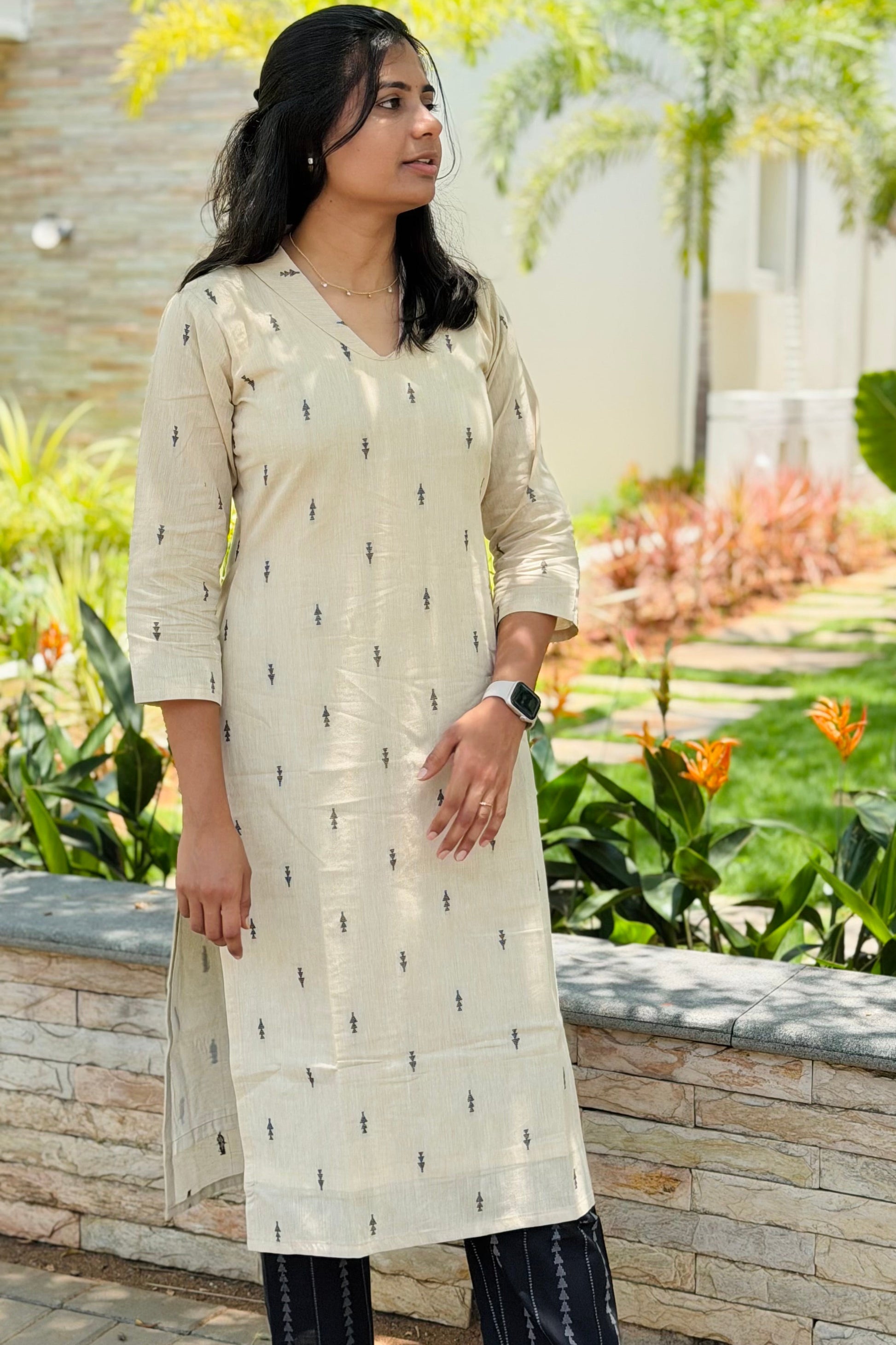 Woman wearing a cream kurta with black pants standing outdoors with greenery in the background