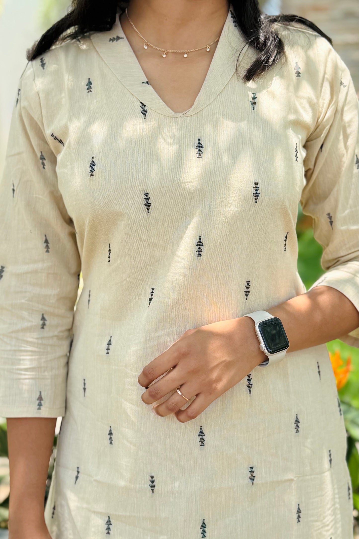 Person wearing a beige kurta with black patterns, standing outdoors.