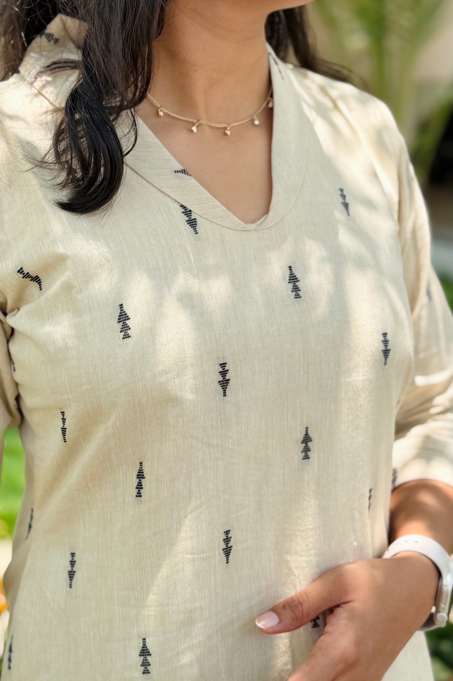 Close-up of a person wearing a light-colored top with black patterns, outdoors.