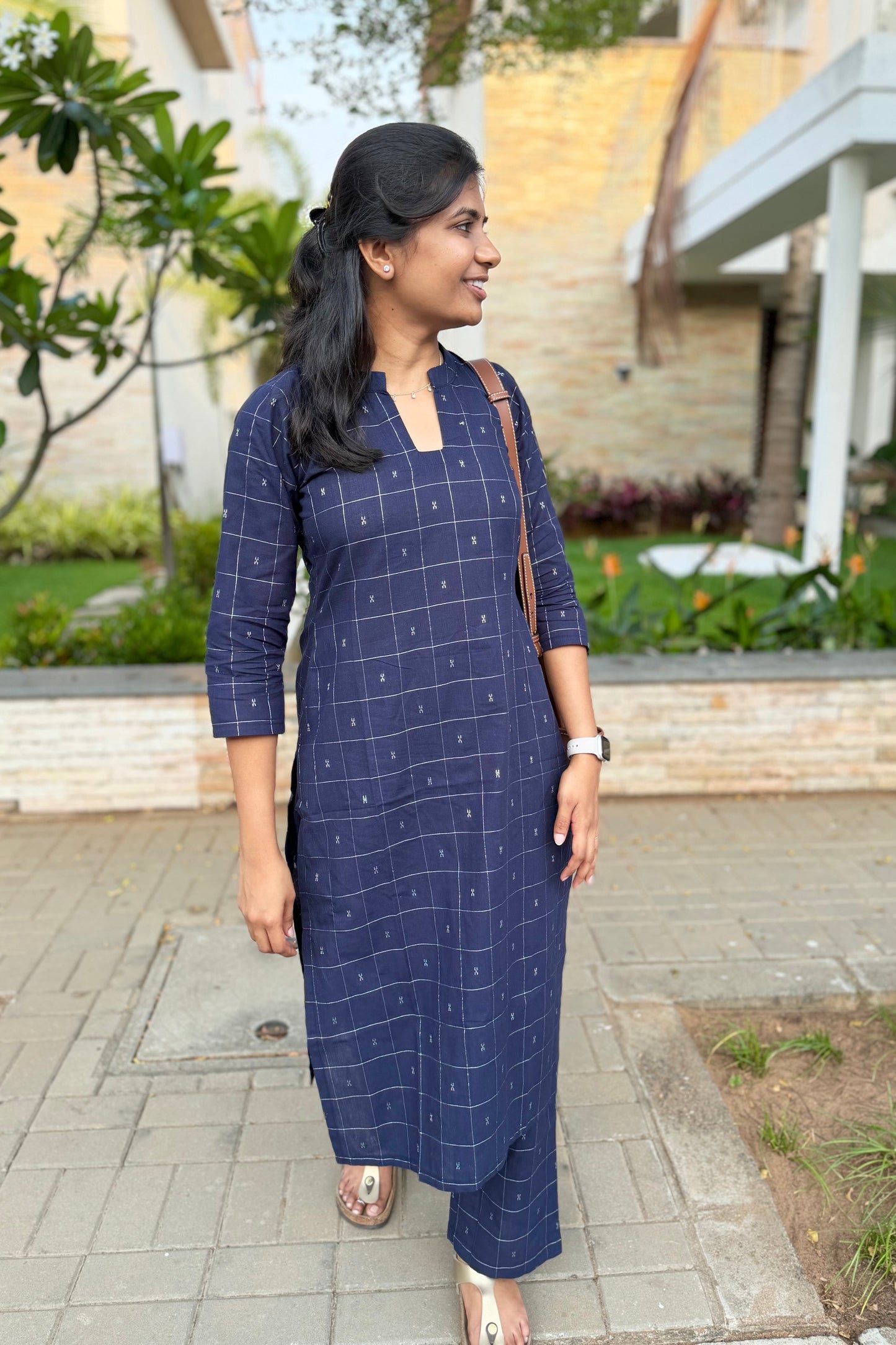 Woman wearing a blue checkered dress standing outdoors on a patio.